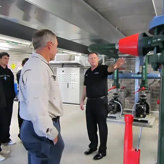 An instructor explains fire safety equipment to staff in a commercial kitchen setting.