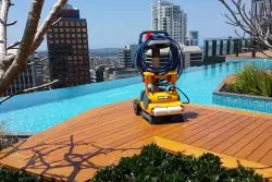 Pool cleaning equipment with hose on rooftop pool deck with city skyline view.