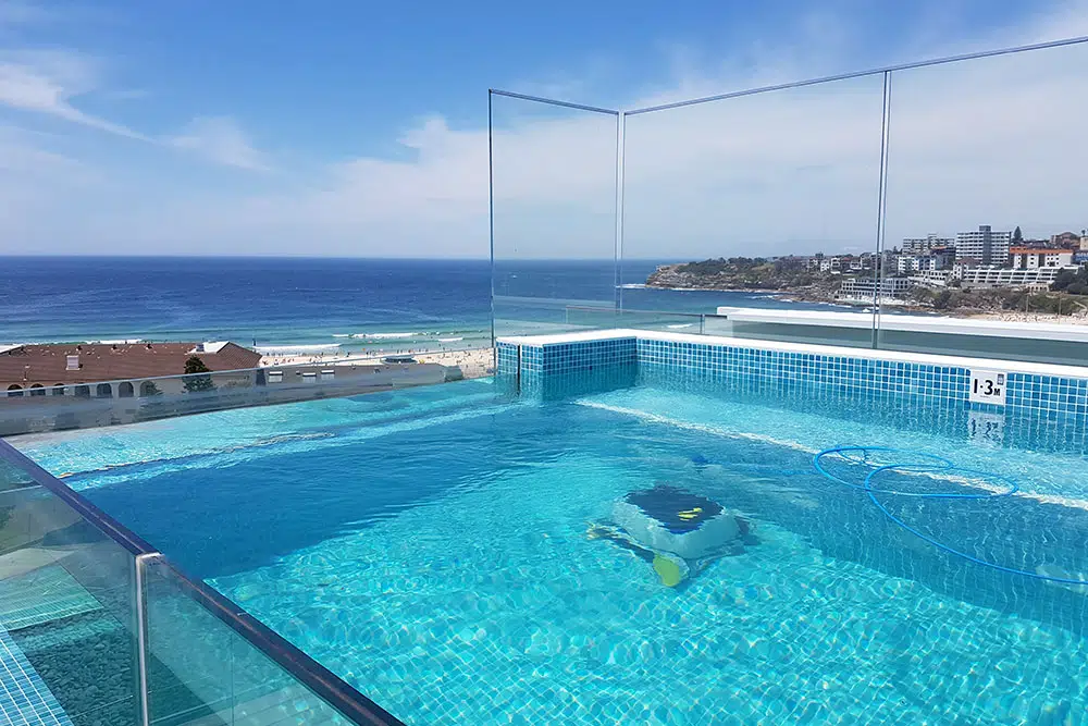 Rooftop infinity pool overlooking Bondi Beach with glass barriers and stunning ocean scenery.